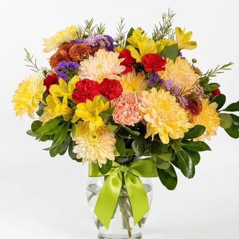 Yellow dahlias, red carnations, and purple accent flowers in a clear glass vase with lime ribbon — Summer Cheer Vase by Florent Floral Newmarket