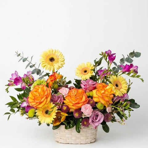 Orange roses, yellow gerbera daisies, and purple alstroemeria in a white wicker basket — Sunrise Garden Basket by Florent Floral Newmarket