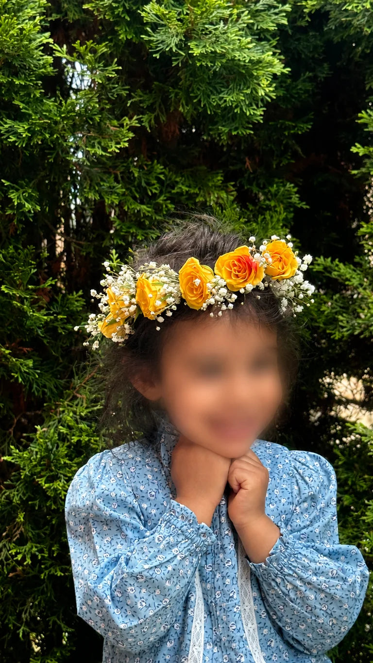 Child wearing a yellow rose flower crown with baby's breath and greenery