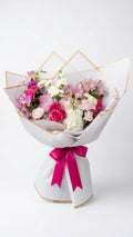 Blush Garden Bouquet with hot-pink roses, carnations, white lisianthus, and alstroemeria wrapped in gold-edged paper with magenta ribbon - Florent Floral Newmarket ON