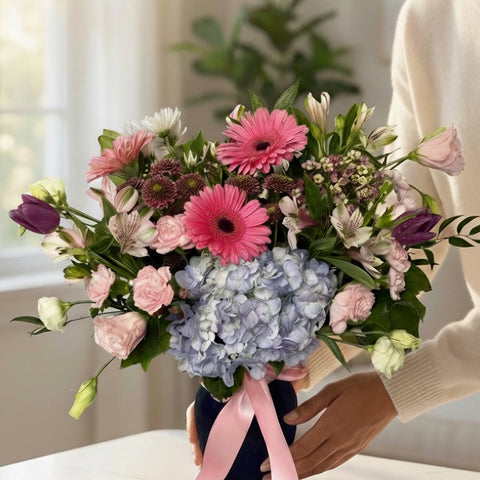 Colourful birthday flower arrangement in navy blue vase with pink ribbon featuring gerbera daisies and hydrangeas - Florent Floral